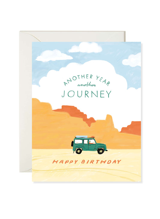 Illustrated birthday greeting card featuring a green Land Rover driving through a desert landscape with “Another Year, Another Journey” text by Karen Schipper.