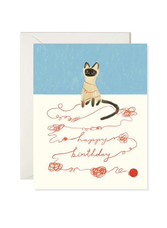 Illustrated birthday greeting card featuring a Siamese cat tangled in red string spelling out “happy birthday” by Karen Schipper.