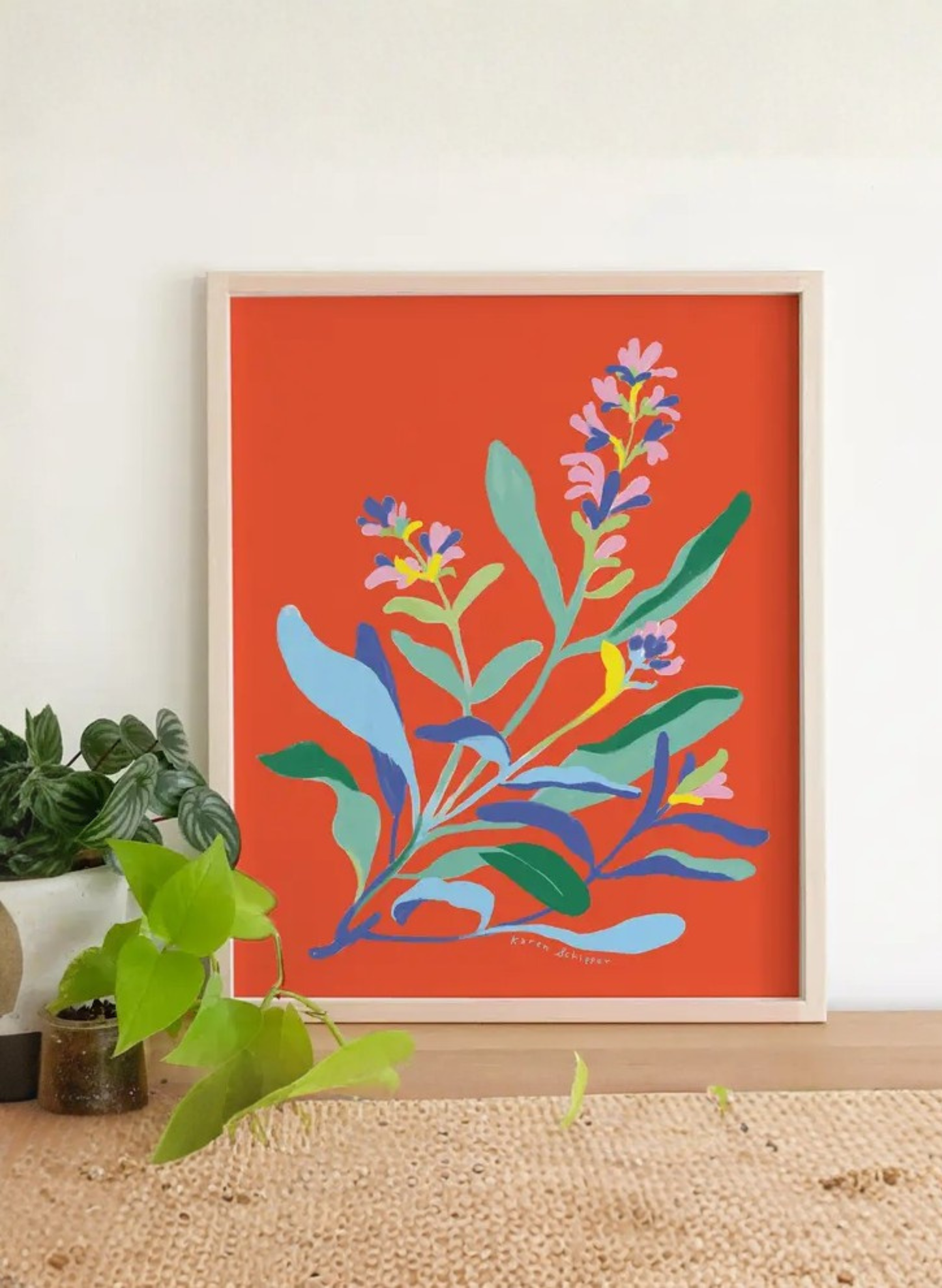 Framed Sage Symphony Art Print by Karen Schipper styled with houseplants, showing colorful botanical wall art on a vivid red background