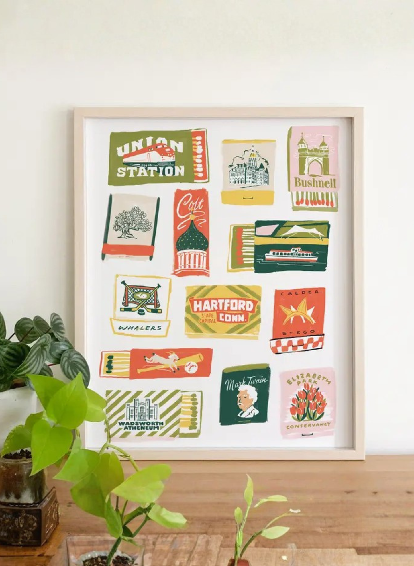 Framed Hartford Matchbook Art Print by Karen Schipper styled beside potted plants, featuring colorful Connecticut city wall art and vintage matchbook details.