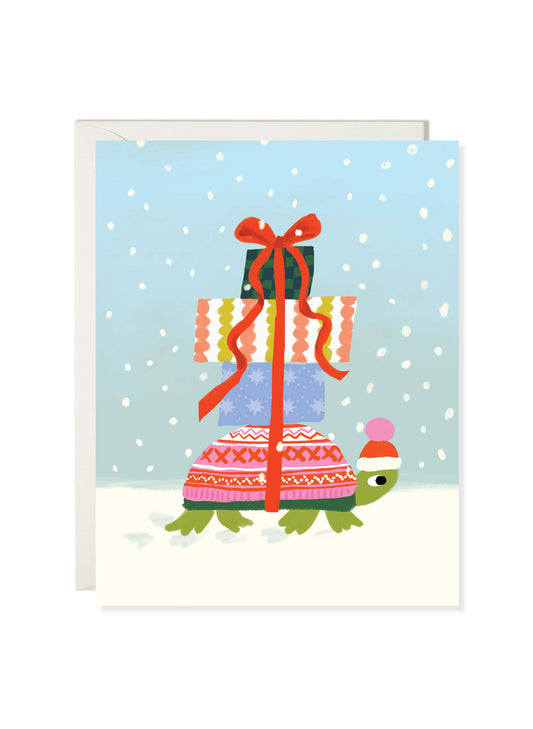Winter Turtle card by Karen Schipper featuring a green turtle in a winter hat and cozy sweater carrying stacked Christmas gifts in the snow.