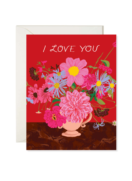 I Love You Flowers Card by Karen Schipper featuring a bold bouquet of pink and blue flowers in a vase on a red background.