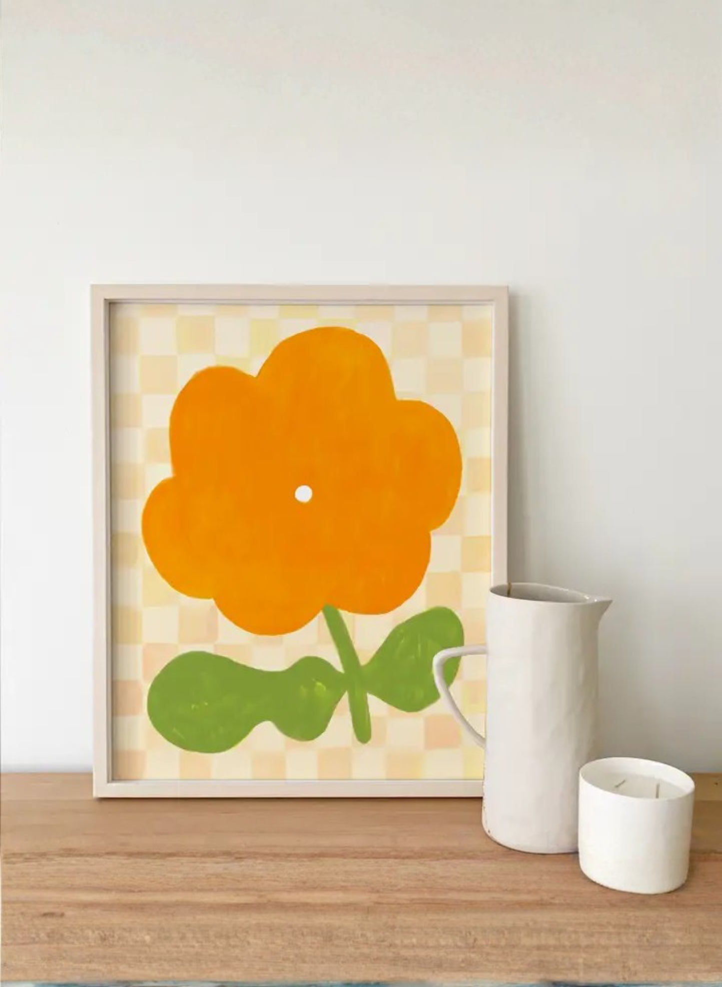 Framed Marigold Bloom Art Print by Karen Schipper styled on a shelf with a white vase and candle, showing bright orange floral wall art.