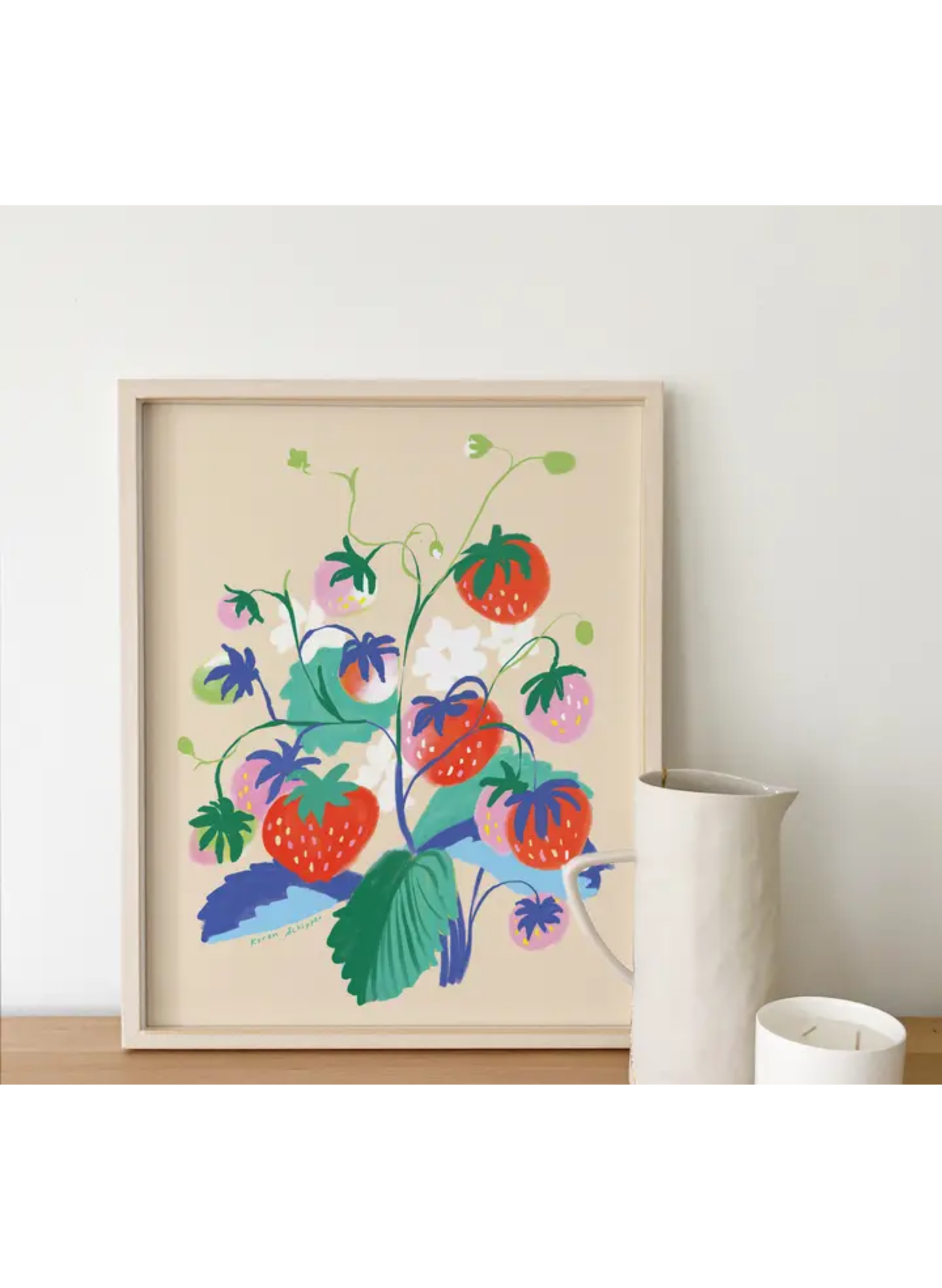 Framed Strawberry Serenade Art Print by Karen Schipper styled on a shelf with a white pitcher and candle, showing colorful fruit wall art.