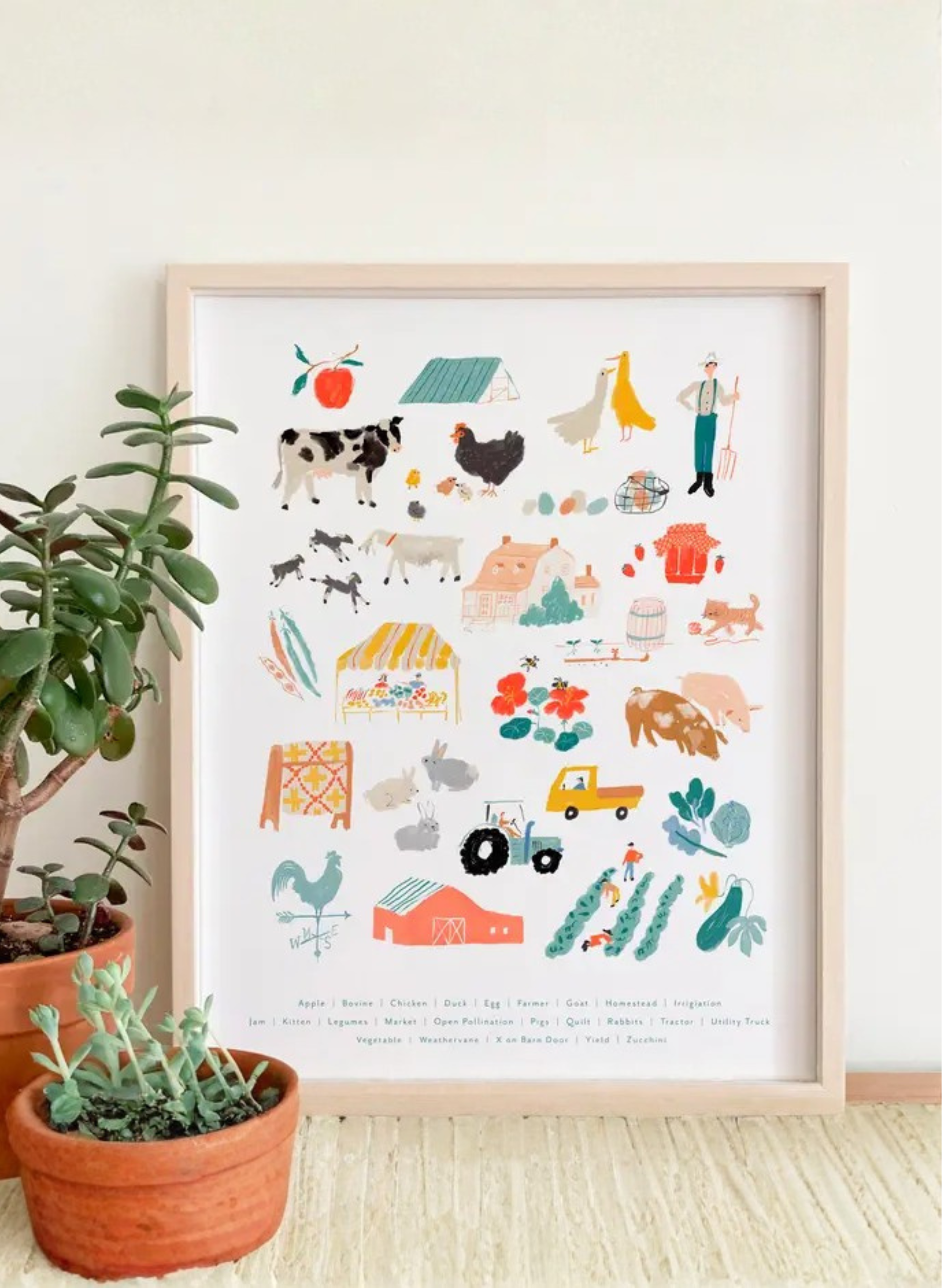 Framed Farm Alphabet Art Print by Karen Schipper styled beside potted plants, showing farm animals, produce, tools, and rural alphabet artwork.