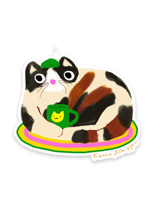 Coffee Cat Sticker by Karen Schipper featuring a calico cat lounging on a colorful rug holding a green coffee mug and wearing a small green hat.